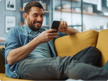 Help support image A man sits on a yellow sofa, looking at his phone and smiling.