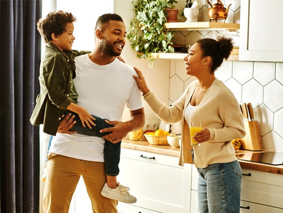 Debt consolidation loans A family stands smiling and chatting in their kitchen.