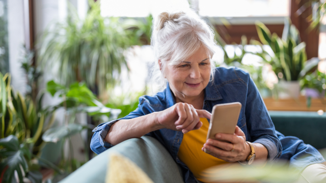 A woman sits on a sofa, typing on her phone.
